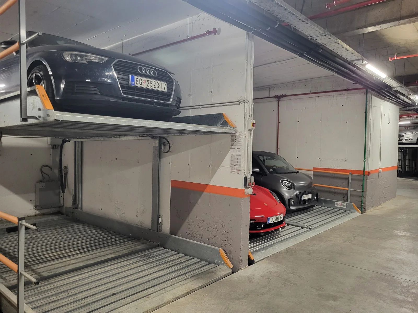 Dva vozila parkirana jedno iznad drugog na hidrauličnoj platformi u garaži stambene zgrade